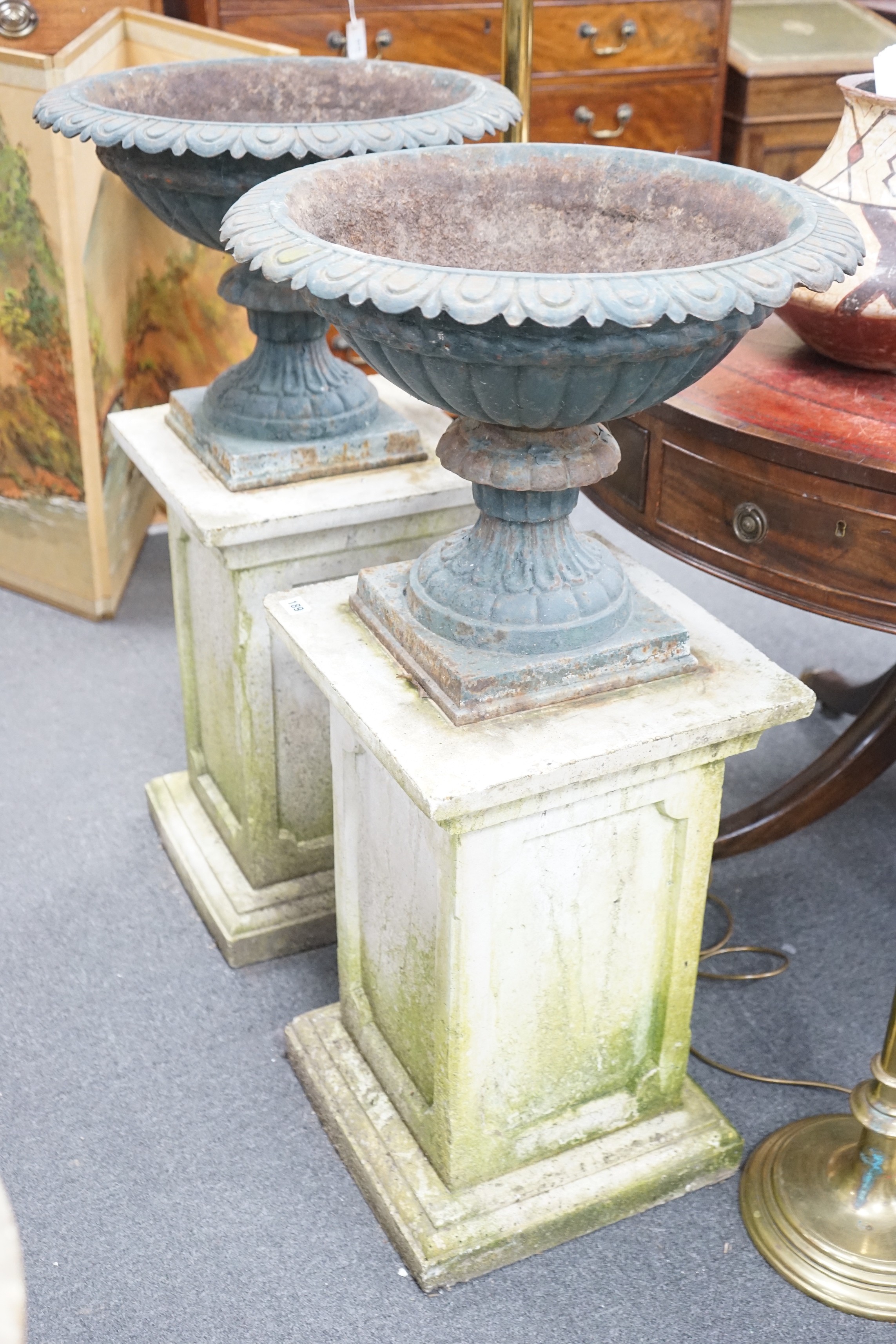 A pair of Victorian painted cast iron campana garden urns on square stone plinths, diameter 51cm, height including plinths 99cm